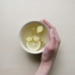 person holding white bowl with sliced lime and ginger inside